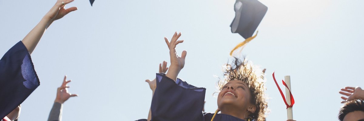 College graduates throwing mortarboards into the air.