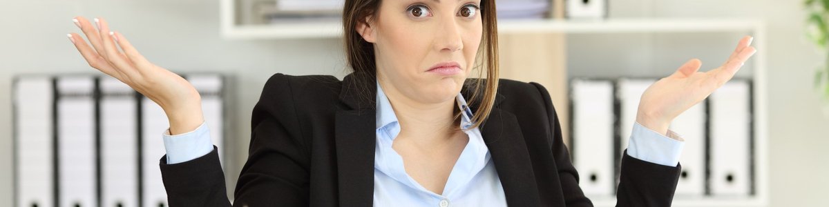 Woman sitting at desk holding her hands up as if confused