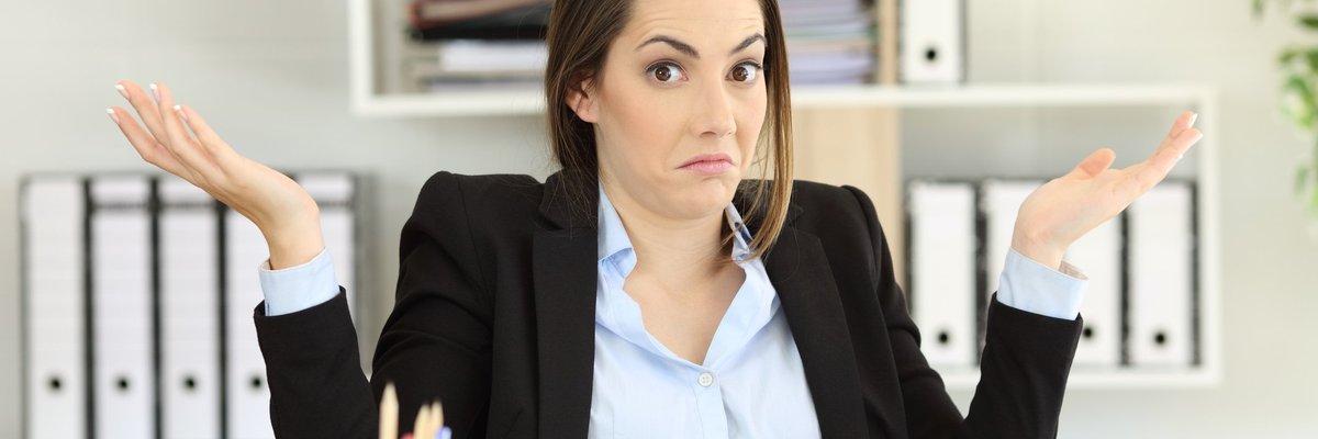 Woman sitting at desk holding her hands up as if confused