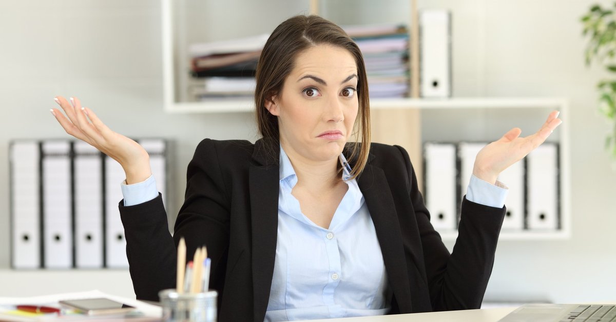 Woman sitting at desk holding her hands up as if confused