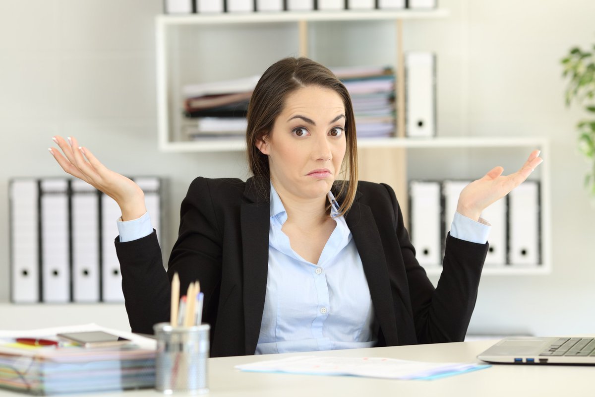 Woman sitting at desk holding her hands up as if confused