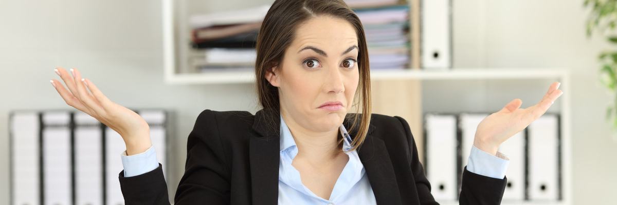 Woman sitting at desk holding her hands up as if confused
