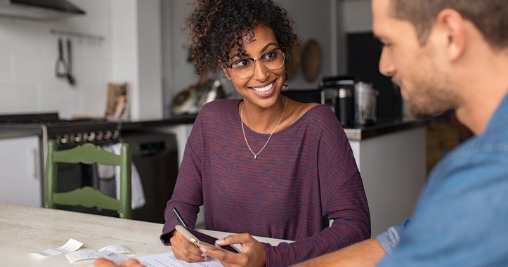 A young woman and man sitting at the kitchen table and looking over paperwork.