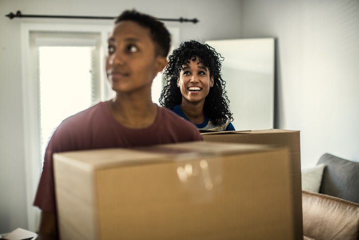 Two women looking around while carrying moving boxes into their new home.