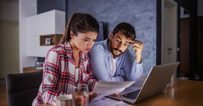 A couple looking worried about money, with a laptop and bills.