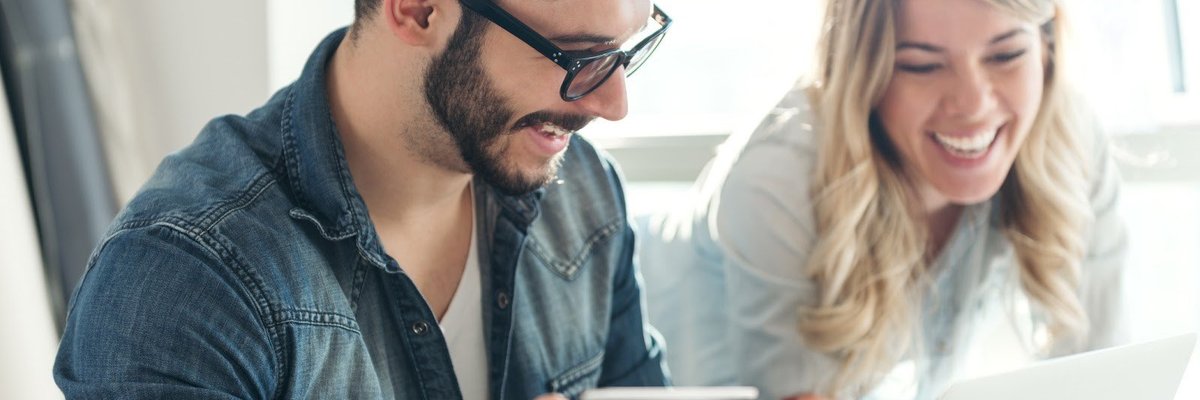 A young couple smiles while looking at a laptop screen and holding a credit card.
