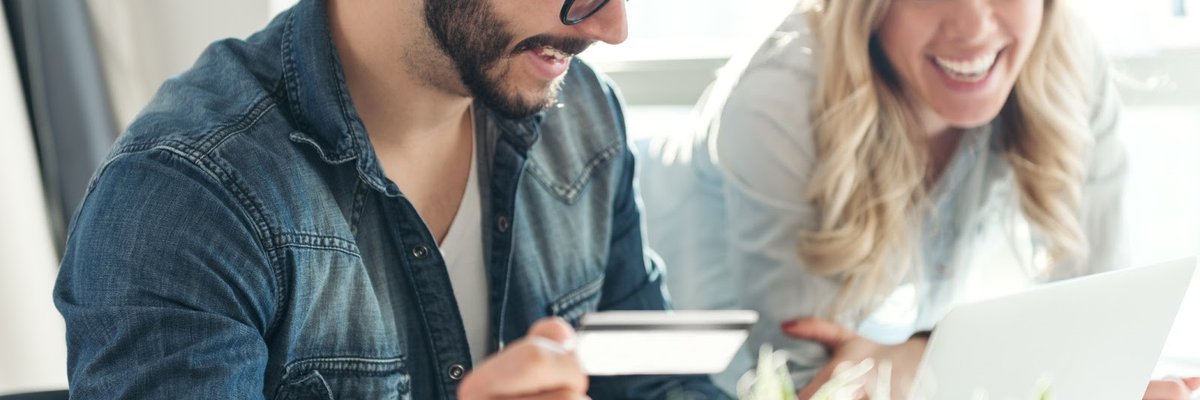 Man holding credit card and looking at computer screen laughing with woman