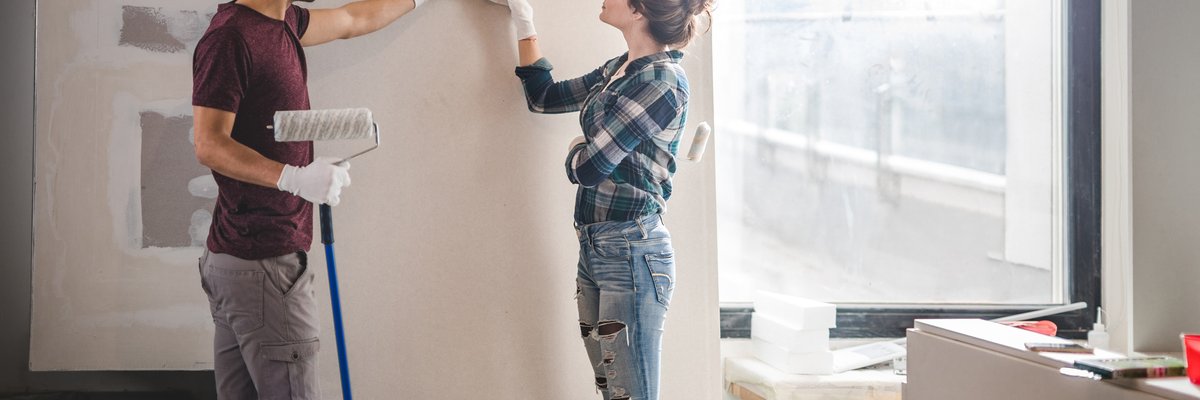 A young couple standing in their home renovation and picking out paint colors.