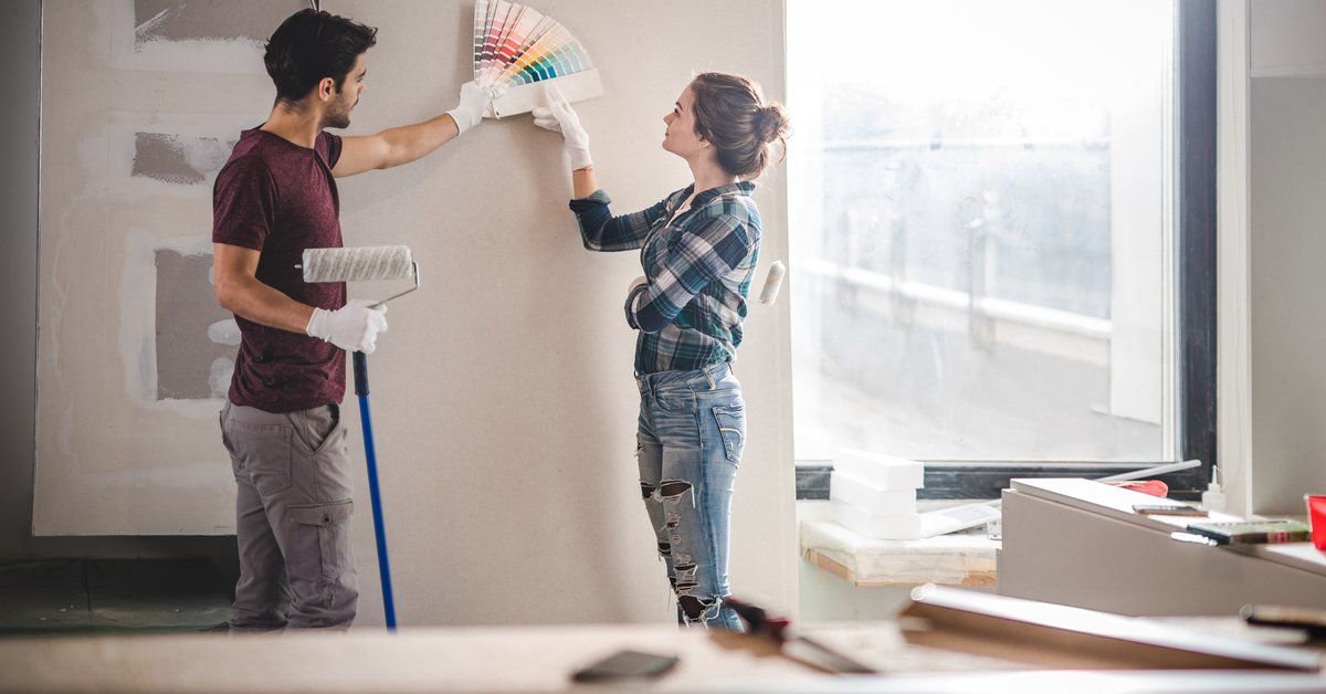 A young couple standing in their home renovation and picking out paint colors.