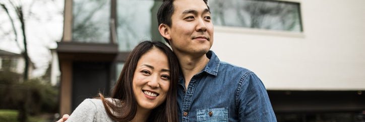 A young man and woman smiling while standing in front of their house.