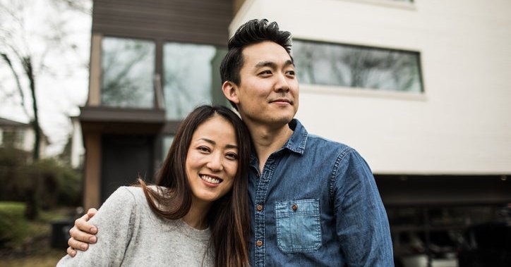 A young man and woman smiling while standing in front of their house.