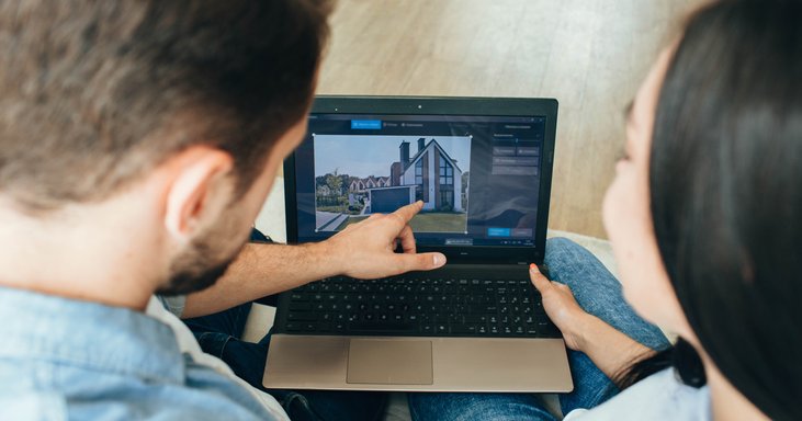 A man and woman sitting next to each other and looking at a house listing on their laptop.
