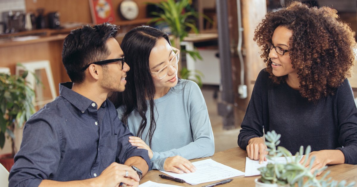 A couple negotiating with a lender at a table with paperwork.