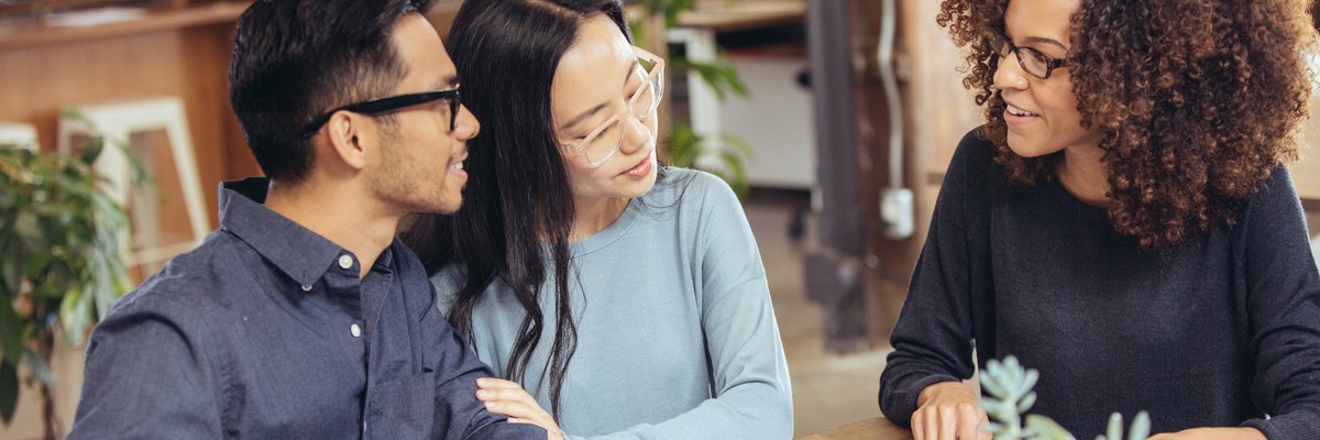 A couple negotiating with a lender at a table with paperwork.
