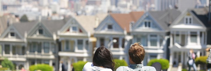 A man and woman lying in the grass in a park on a sunny day facing the Painted Ladies houses in San Francisco.