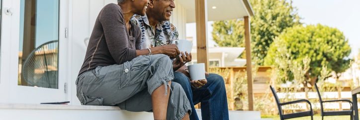 A man and woman smiling while sitting on the steps of their house facing the backyard.