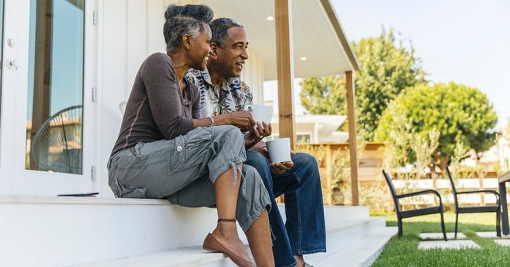 A man and woman smiling while sitting on the steps of their house facing the backyard.