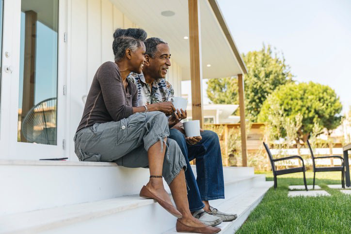 A man and woman smiling while sitting on the steps of their house facing the backyard.