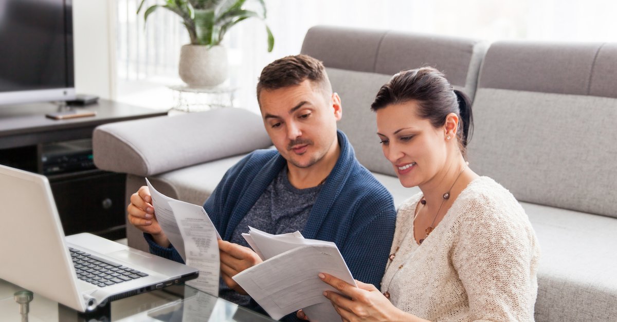 A couple sitting on the floor of their living room organizing paperwork.