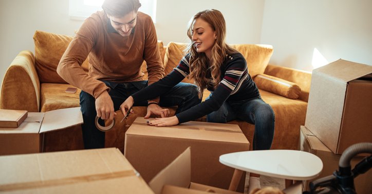 A man and woman sitting on the couch in their living room and packing up moving boxes.
