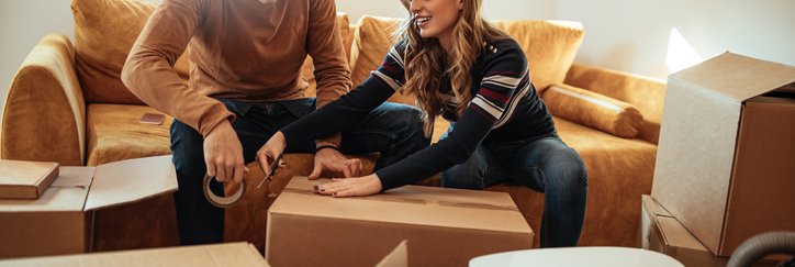 A man and woman sitting on the couch in their living room and packing up moving boxes.