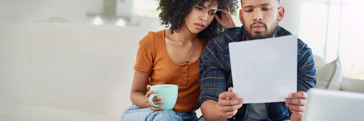 A couple looking distraught while reading bills on their couch.