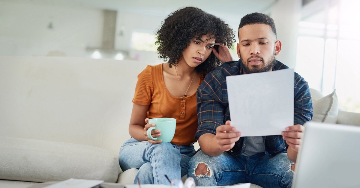 A couple looking distraught while reading bills on their couch.