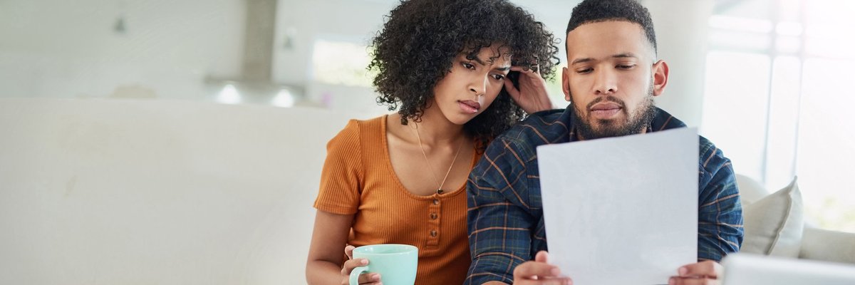 A couple looking distraught while reading bills on their couch.