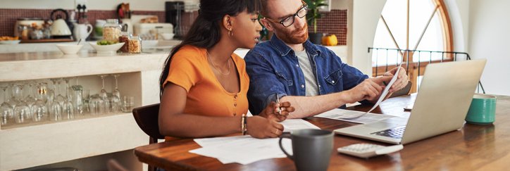 A couple reviewing bills together on a laptop while sitting in their kitchen.