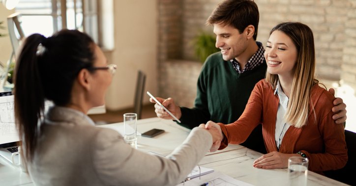 A man and woman signing financial documents while sitting at a desk and shaking hands with a business professional.