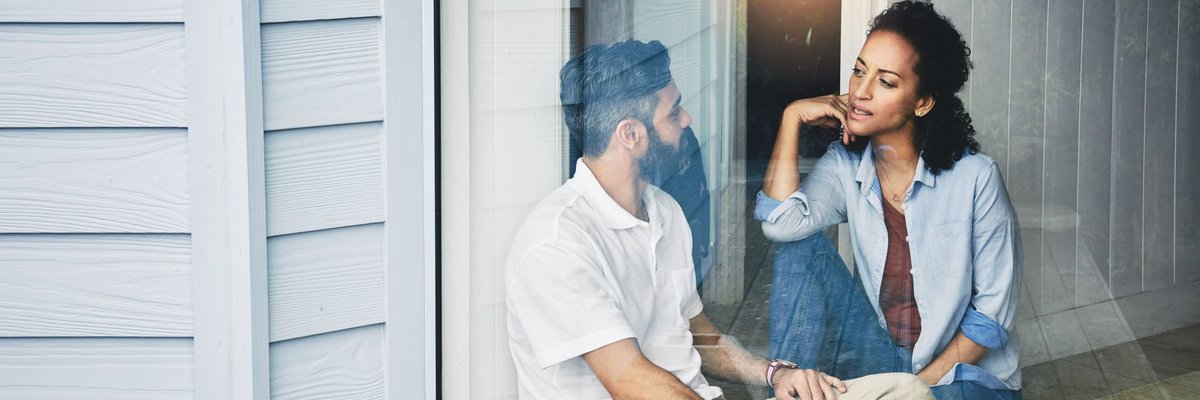 A young couple having a conversation while sitting on the floor in front of a sunny window.
