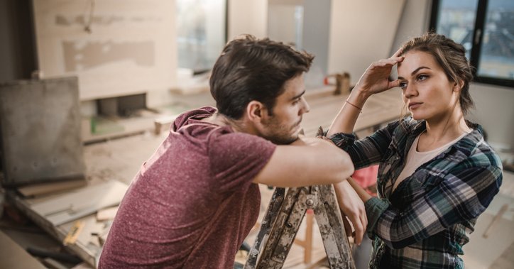 A stressed-looking couple pausing work on renovating their living room.