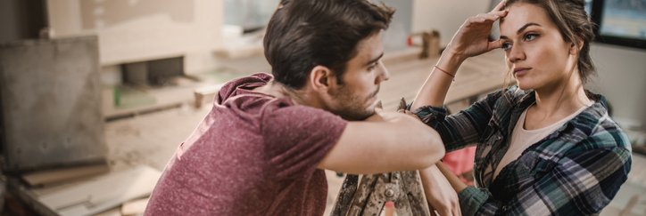 A stressed-looking couple pausing work on renovating their living room.