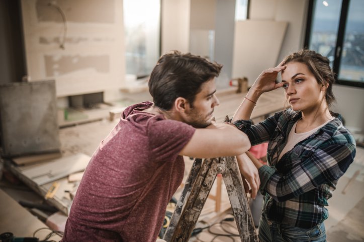 A stressed-looking couple pausing work on renovating their living room.
