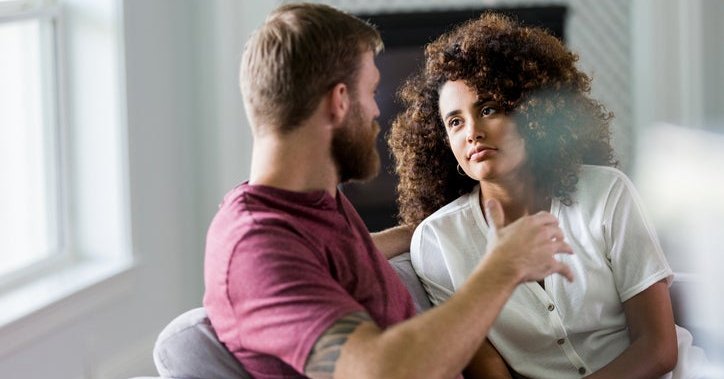 A man and woman sitting on a couch and having a serious conversation.
