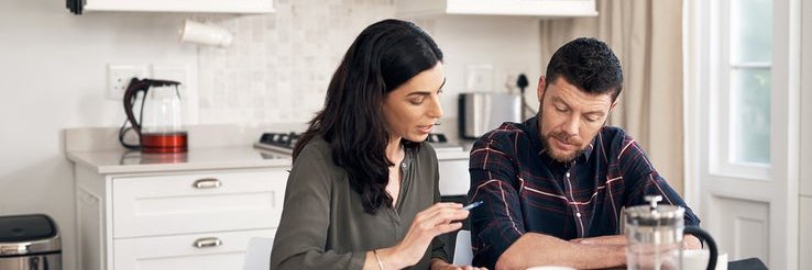 A man and woman sitting in their kitchen and talking while looking over papers.