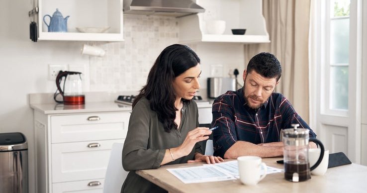 A man and woman sitting in their kitchen and talking while looking over papers.