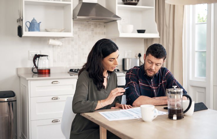 A man and woman sitting in their kitchen and talking while looking over papers.