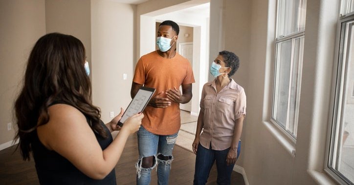 A man and woman wearing medical masks while touring an empty home with their realtor.