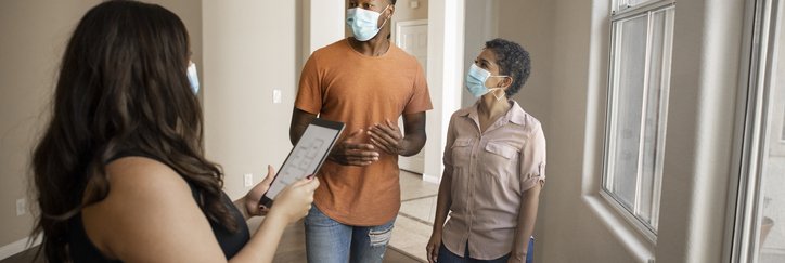 A man and woman wearing medical masks while touring an empty home with their realtor.