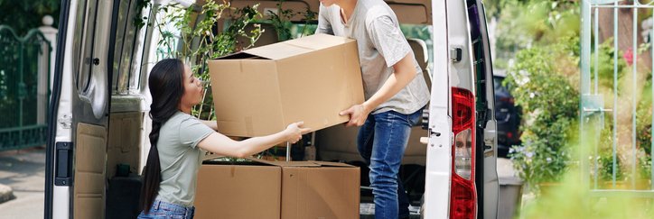 A man and woman unloading boxes from the back of a moving van.