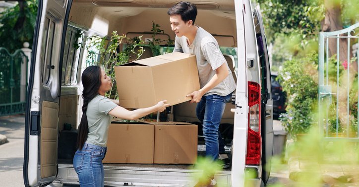 A man and woman unloading boxes from the back of a moving van.