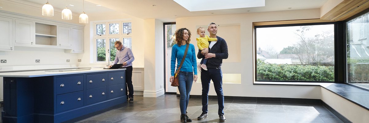A couple holding their baby while walking through an empty eat-in kitchen with their realtor.