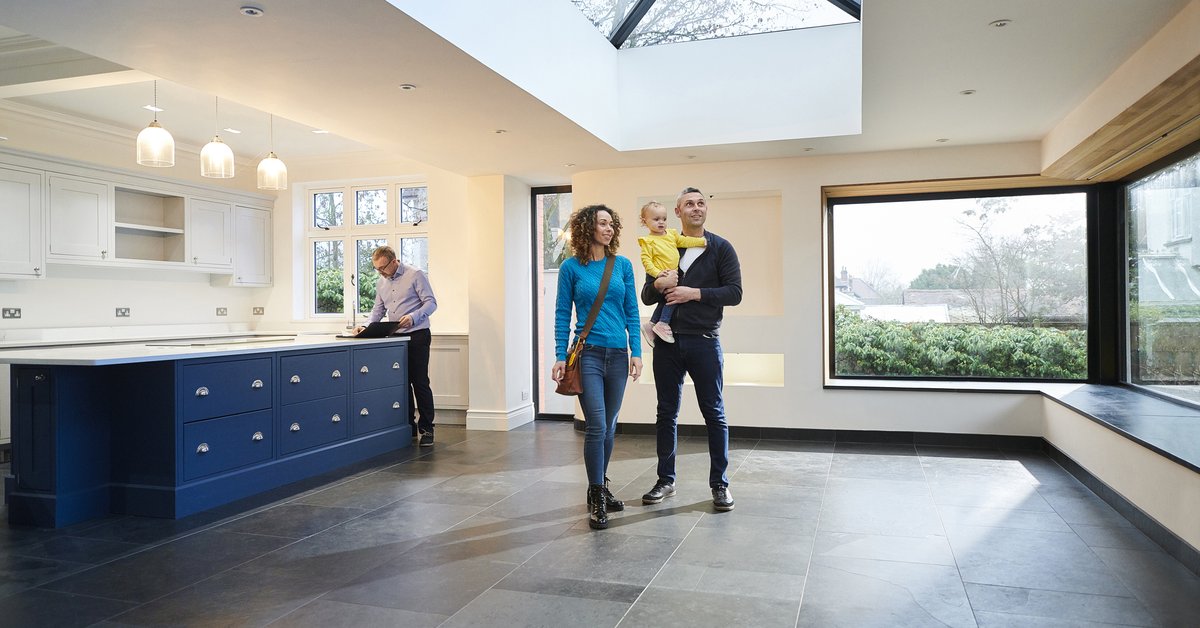 A couple holding their baby while walking through an empty eat-in kitchen with their realtor.