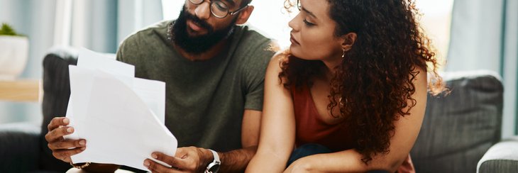 A man and woman sitting on their couch looking through bills and signing papers.