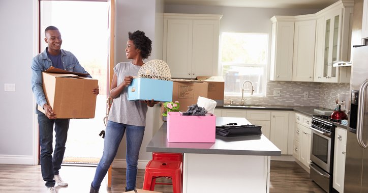 A man and woman carrying boxes into the kitchen of their new home.
