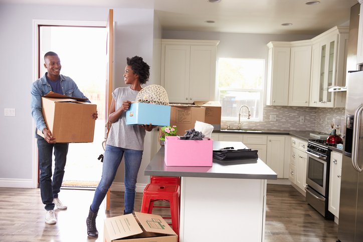 A man and woman carrying boxes into the kitchen of their new home.