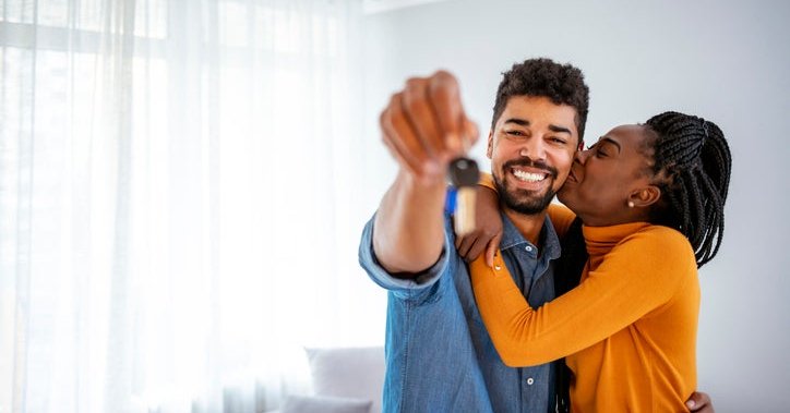 A woman kissing a man on the cheek while he holds up house keys.