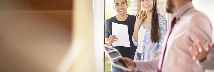 A man and woman looking through the door of a house held open by a realtor.