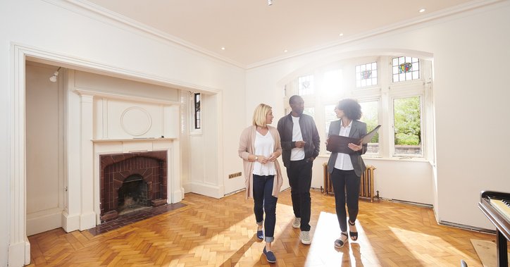 A couple speaking with their realtor while looking around the empty living room of a home.